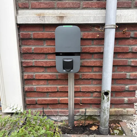 Peblar laadpaal op een paal tegen de bakstenen gevel van een woning in Bunschoten