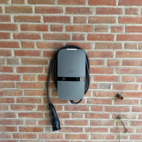 Laadpunt met laadkabel aan een rode bakstenen gevel in Hilversum