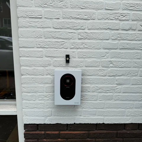Wit Zaptec laadpunt aan een witgeschilderde gevel in Nijkerk